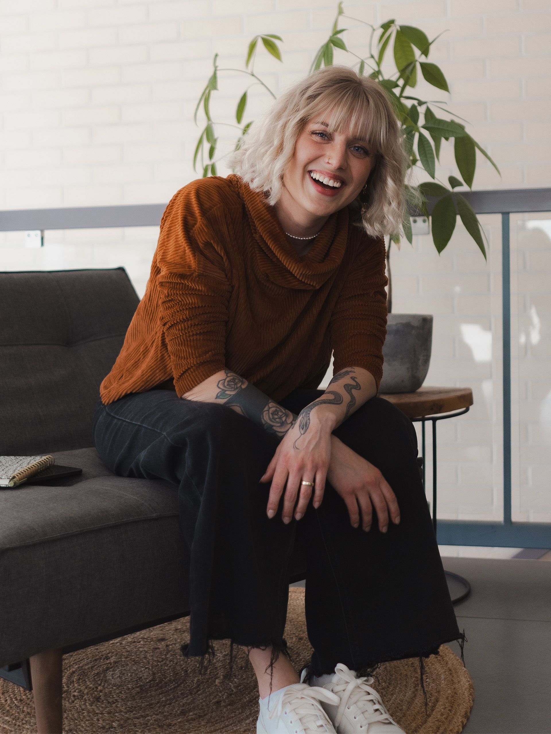 Paula Sembritzki – Expertin für strategisches Webdesign – sitzt im Gespräch auf einem grauen Sofa und zeigt Persönlichkeit durch authentisches lachen.