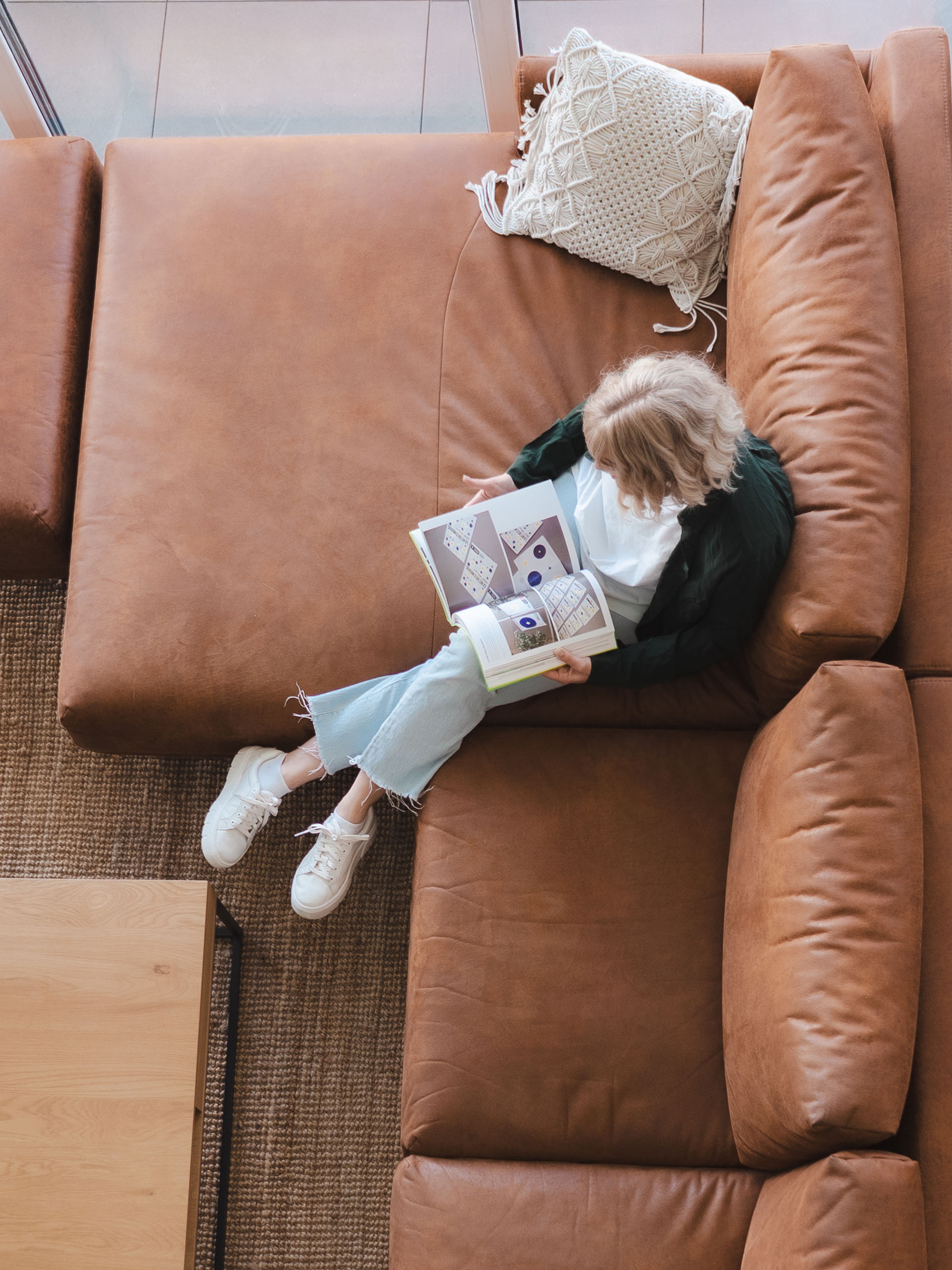 Paula Sembritzki in Vogelperspektive mit offenem Design-Buch auf dem Sofa – authentisches Bild der Gründerin von straight out | designstudio.