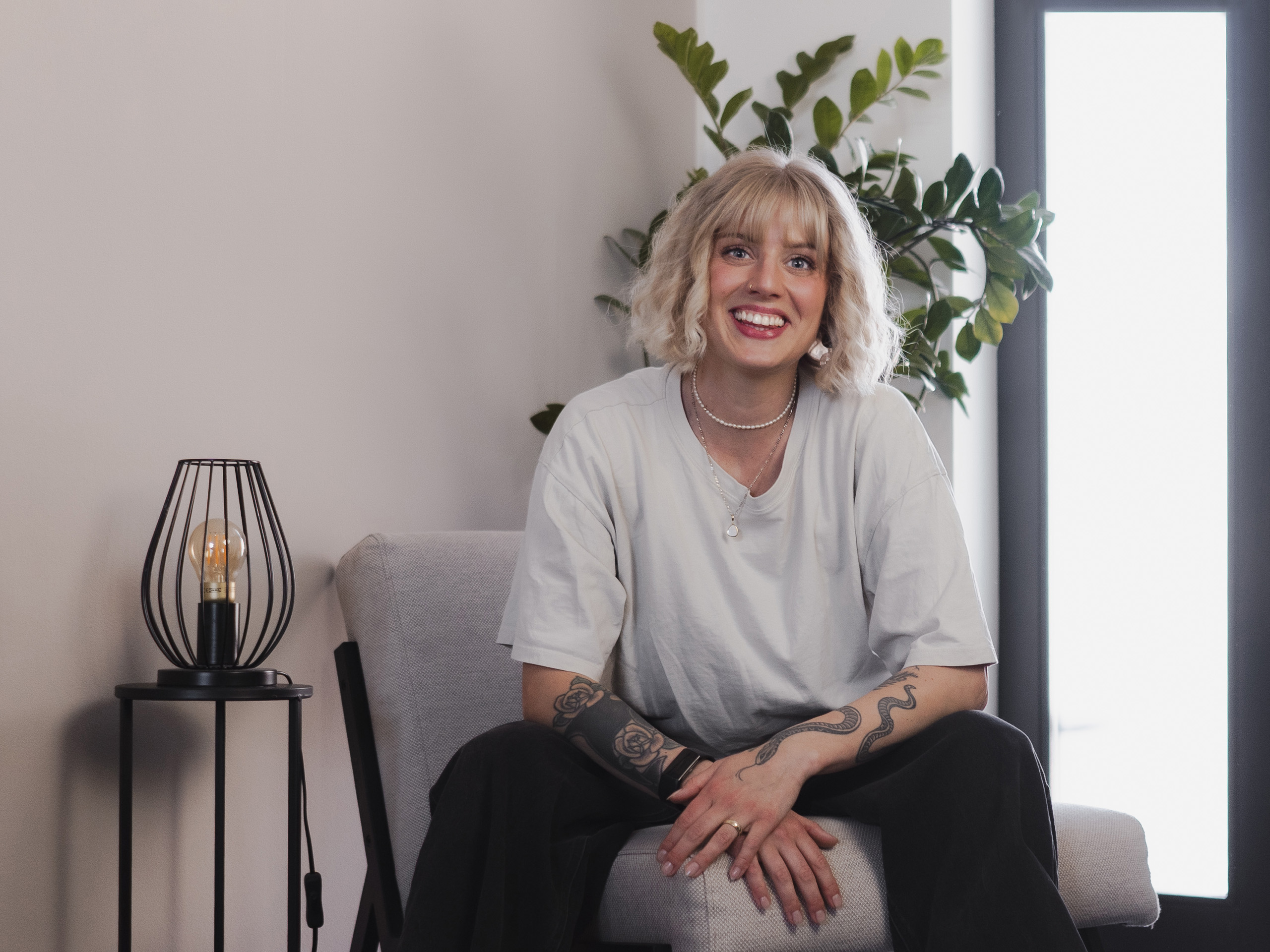 Paula Sembritzki – Gründerin von straight out | designstudio – sitzt in heller Umgebung auf einem Stuhl und vermittelt mit ihrer Haltung professionelles, authentisches Auftreten durch ein offenes Lachen.